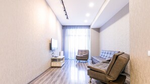 A modern living room with a flat-screen TV, a sofa, a chair, and a wooden TV stand. - Apartment on Saakadze Square (Tbilisi)