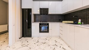 A modern kitchen with white cabinets, a black tiled backsplash, and a marble floor. - Apartment on Saakadze Square (Tbilisi)