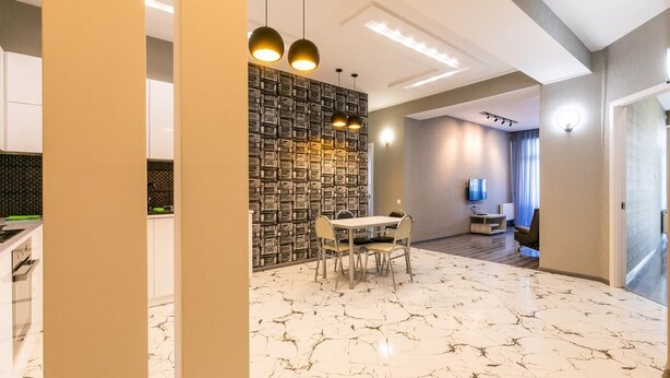 A modern interior with a marble floor, a dining area with a table and chairs, and a kitchen with white cabinets. - Apartment on Saakadze Square (Tbilisi)