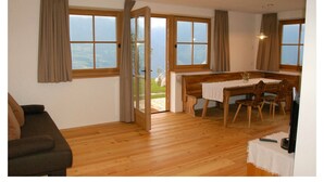 A room with wooden flooring, a dining table with chairs, a bench, and a sofa. - Tholer (Lagundo)