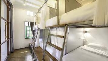 A train compartment with bunk beds, a ladder, and a window with curtains.