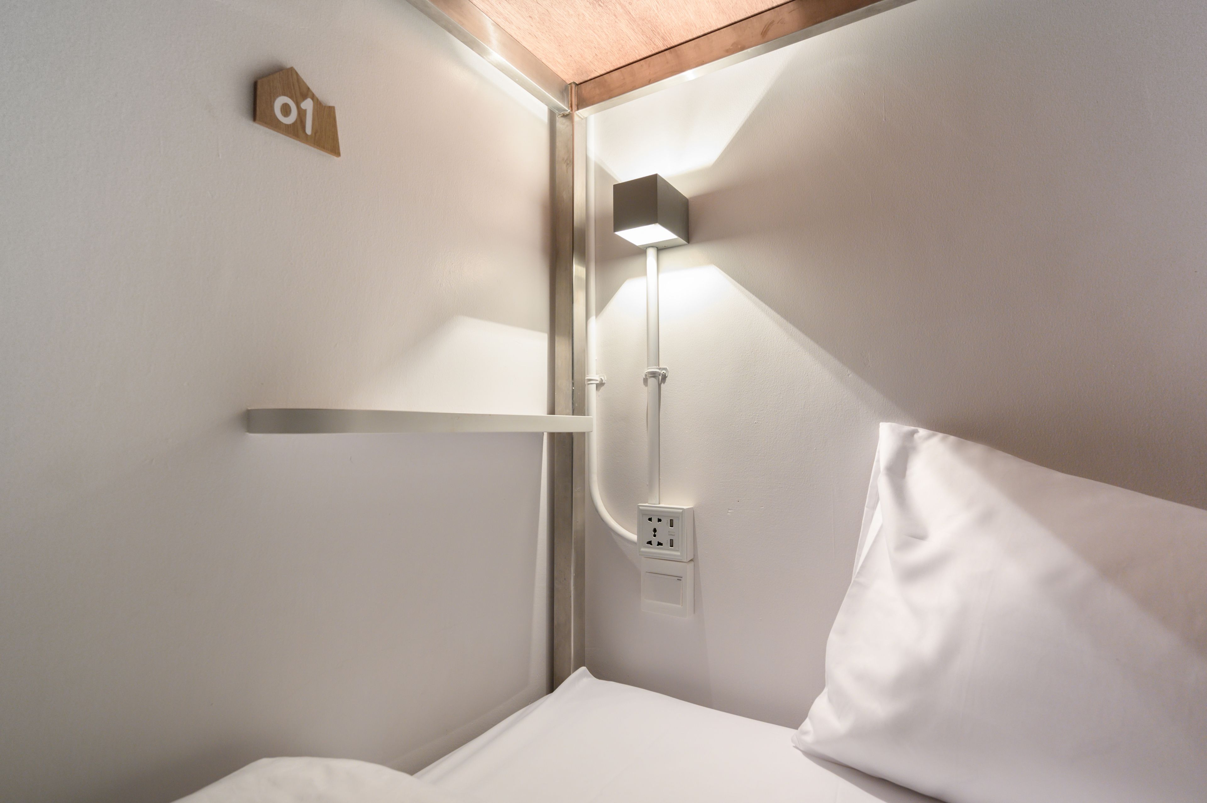 Una habitación pequeña y bien iluminada con una cama, una repisa y un aplique de pared.