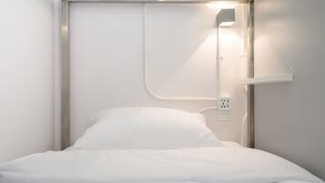 A single bed with white bedding in a room with white walls and a metal frame.