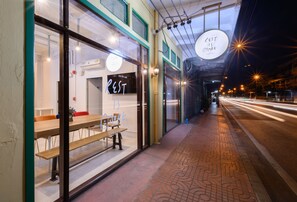 A hostel with a wooden bench outside, a sign reading "REST IS MORE HOSTEL", and a patterned sidewalk. - REST IS MORE Hostel (Bangkok)