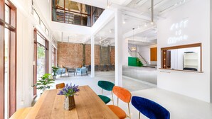 A spacious, modern interior with a wooden table and colorful chairs, a brick wall, and a sign that reads "REST IS MORE". - REST IS MORE Hostel (Bangkok)
