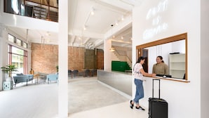 A spacious lobby with a high ceiling, exposed brick walls, and a modern reception desk. - REST IS MORE Hostel (Bangkok)