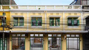 A yellow building with green shutters and a sign that reads "REST IS HERE". - REST IS MORE Hostel (Bangkok)