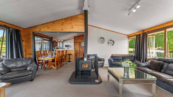 A spacious living area with a fireplace, leather sofas, a dining table, and a kitchen in the background.