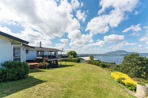 A house with a deck, a lawn, and a view of a lake and mountains. - Heights Haven - Acacia Bay Holiday Home (Acacia Bay)