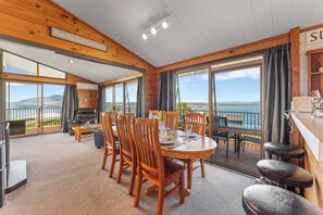 A wooden interior with a dining area, large windows, and a view of the sea. - Heights Haven - Acacia Bay Holiday Home (Acacia Bay)
