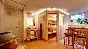 Une salle de bain moderne dotée d’une douche à parois de verre, d’un meuble-lavabo en bois et d’un coin salon avec une table et des chaises.