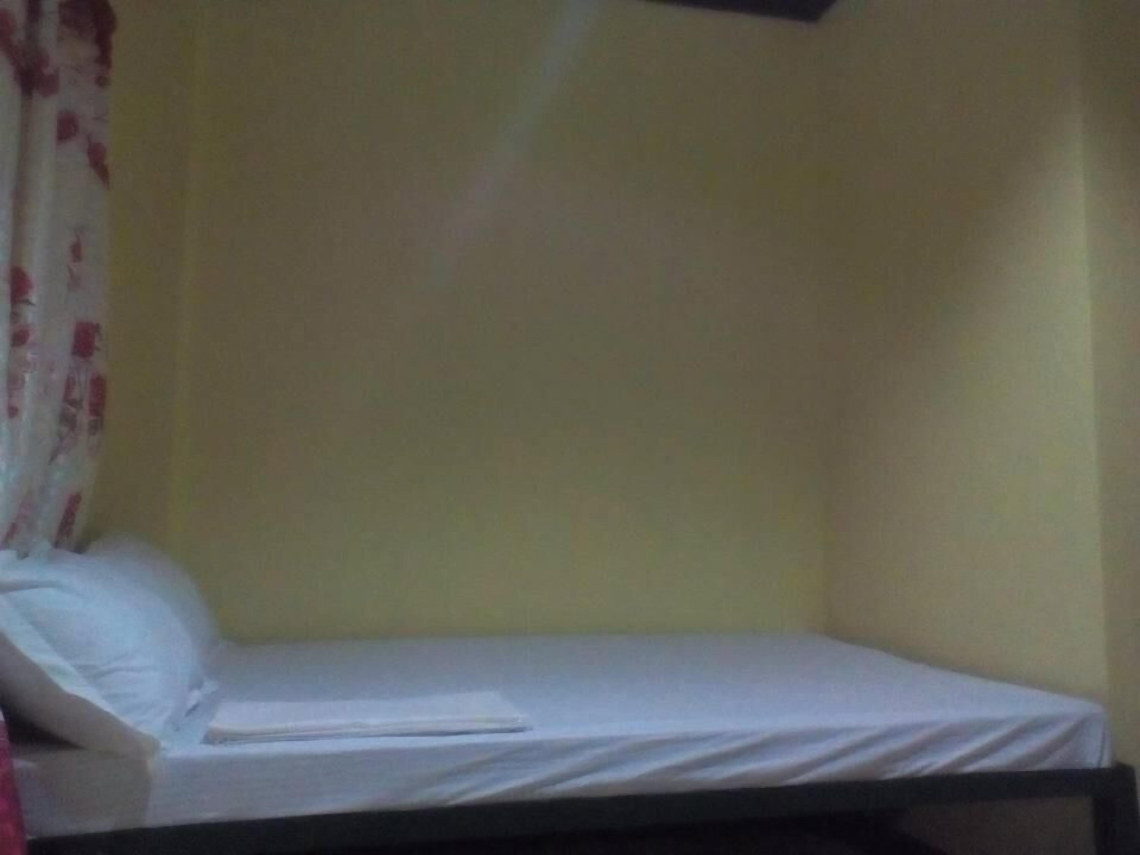 A small, single-bed room with a plain white mattress and a single pillow.