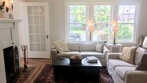 A living room with a white sofa, a coffee table, a patterned rug, a fireplace, and a view of the outside.