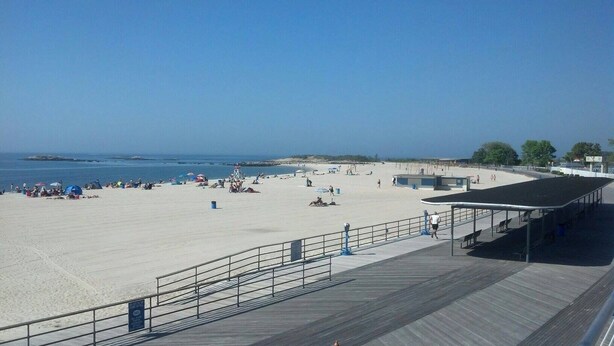 A beach with a wooden boardwalk, umbrellas, and people.
