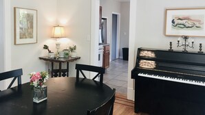 A dining area with a piano, a table with chairs, a lamp, and a vase of flowers.
