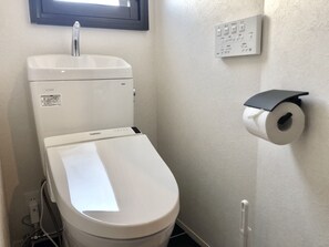 A toilet with a TOTO brand label, a wall-mounted flush handle, a toilet paper holder, and a window above the sink.