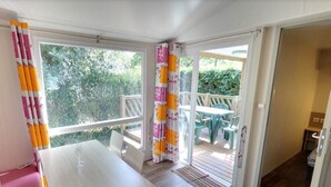A room with a wooden table and chairs, a window with curtains, and a door leading to an outdoor area with a table and chairs.