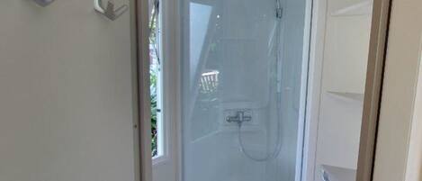 A glass-enclosed shower with a white door, a small window, and a white sink with a cabinet below.