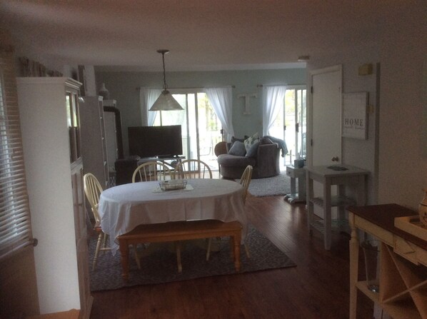 A dining area with a table and chairs, a television in the background, and a sofa in the living room.