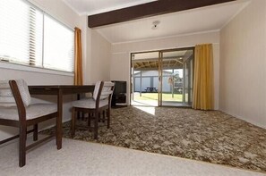 A room with a dining table and chairs, a patterned carpet, a sliding glass door leading outside, and a ceiling with exposed beams.