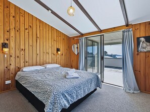 Une chambre avec un grand lit, des murs en bois, une porte-fenêtre coulissante et un luminaire au plafond.