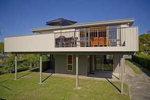 A modern two-story house with a balcony, a covered patio, and a large window. - Joes Place - Cooks Beach Holiday Home (Cooks Beach)
