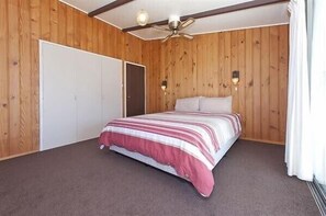 A bedroom with a bed, wooden walls, a ceiling fan, and a wardrobe.