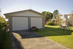 A single-story building with a garage and a small patio area. - Joes Place - Cooks Beach Holiday Home (Cooks Beach)