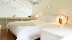 Een slaapkamer met een schuine kap, een bed met witte lakens, een nachtkastje met een lamp, en een kleine plant op het nachtkastje.