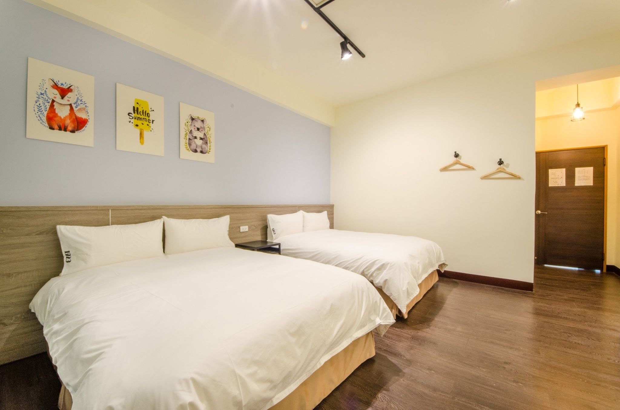 A hotel room with two beds, a wooden headboard, a light blue wall, and three framed pictures.