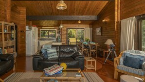 A cozy log cabin interior with a living room, dining area, and kitchen. - Norma's Place - Simpsons Beach Bach (Whitianga)