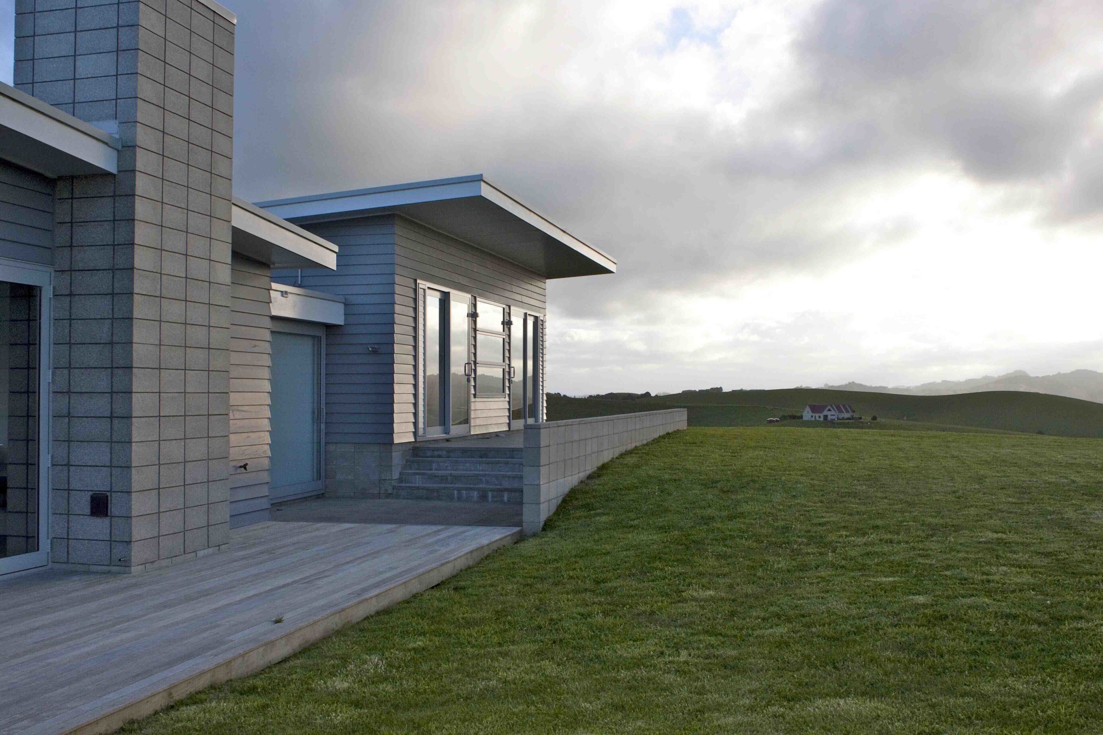 A modern house with a large deck, a covered porch, and a grassy yard.