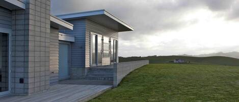 A modern house with a large deck, a covered porch, and a grassy yard.
