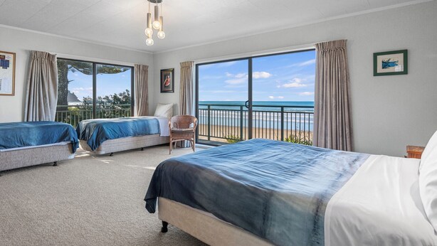 Ein Hotelzimmer mit zwei Betten, einem Sessel, einem Balkon mit Blick auf den Strand und einer Deckenleuchte.
