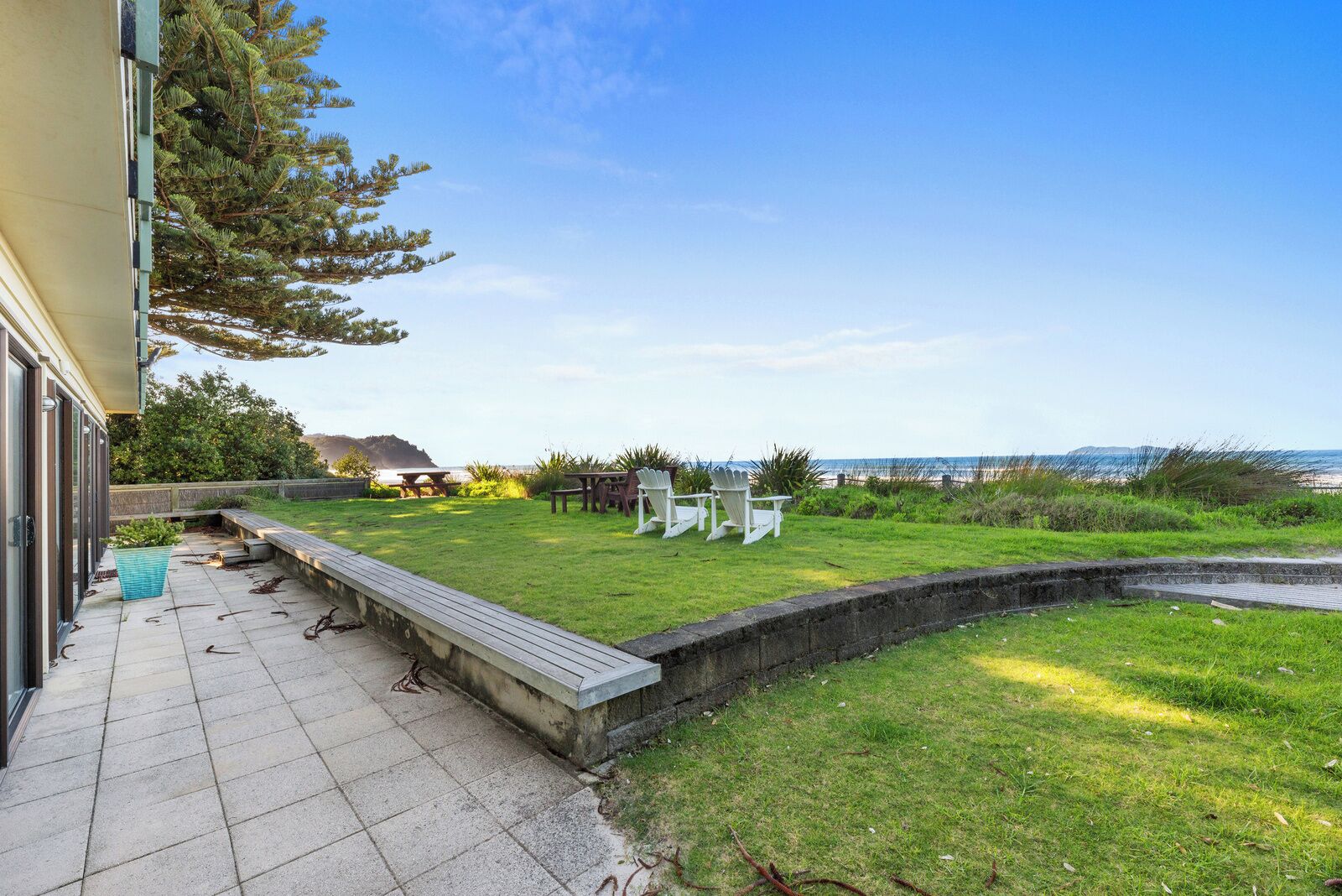 Un patio con vista sull'oceano, una zona verde con sedie e un pontile in legno.
