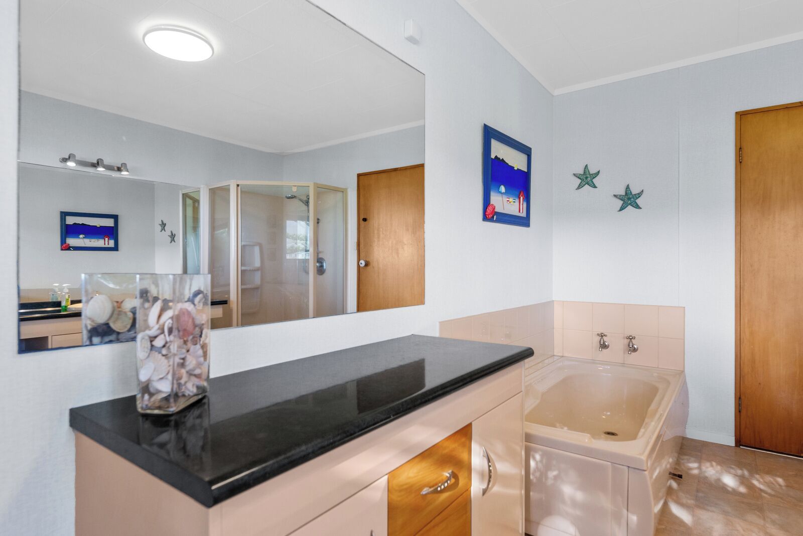 A modern bathroom with a large mirror, a bathtub, and a vanity with a sink.