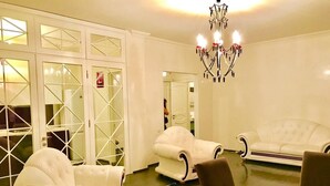 Un vaste salon doté de canapés en cuir blanc, d’une cloison en verre et d’un lustre.