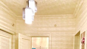 Un couloir avec deux portes blanches, dont une est ouverte et donne sur une salle de bain équipée d’une douche et d’un porte-serviettes.