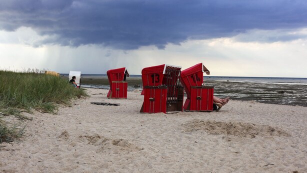 A beach with red beach chairs and a white chair.
