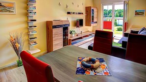 A modern living room with a dining table, red chairs, a bookshelf, and a view of the outdoors.