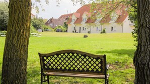 A bench in a grassy area with trees and houses in the background.