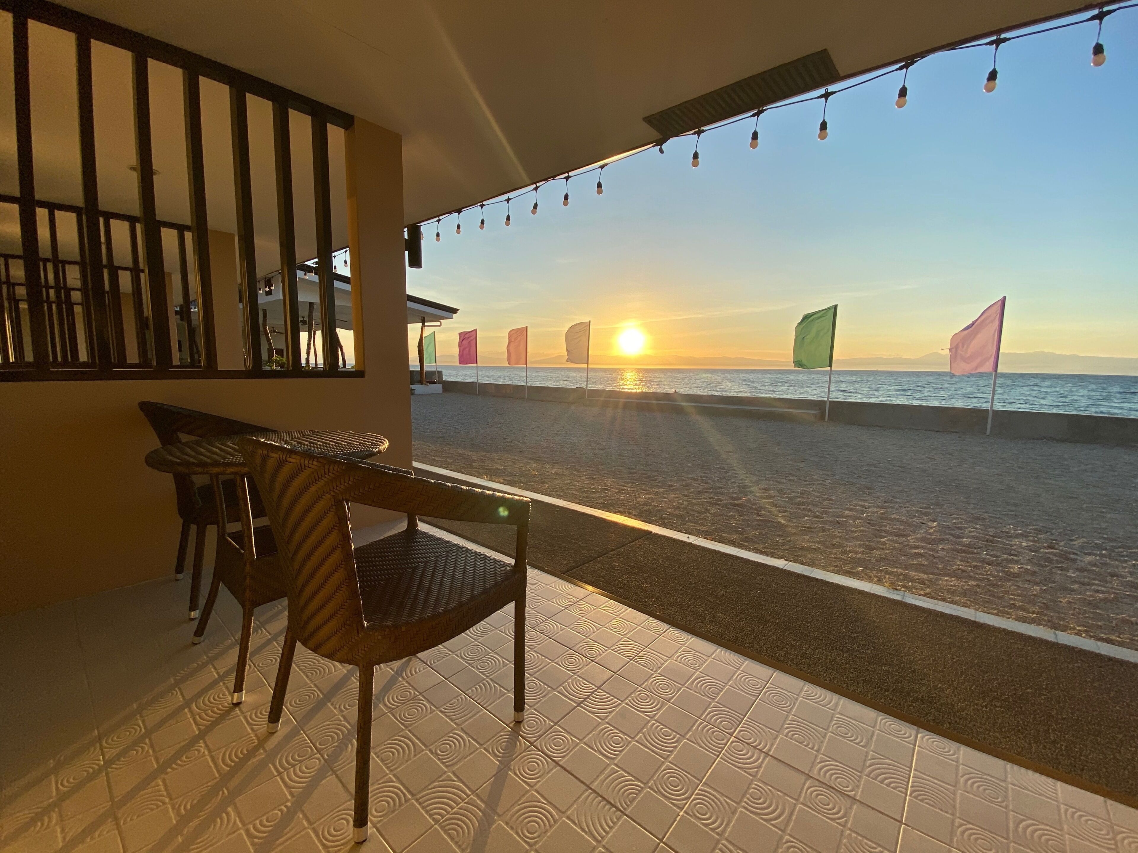 A balcony with a view of the sunset over the sea, a chair, and a table.