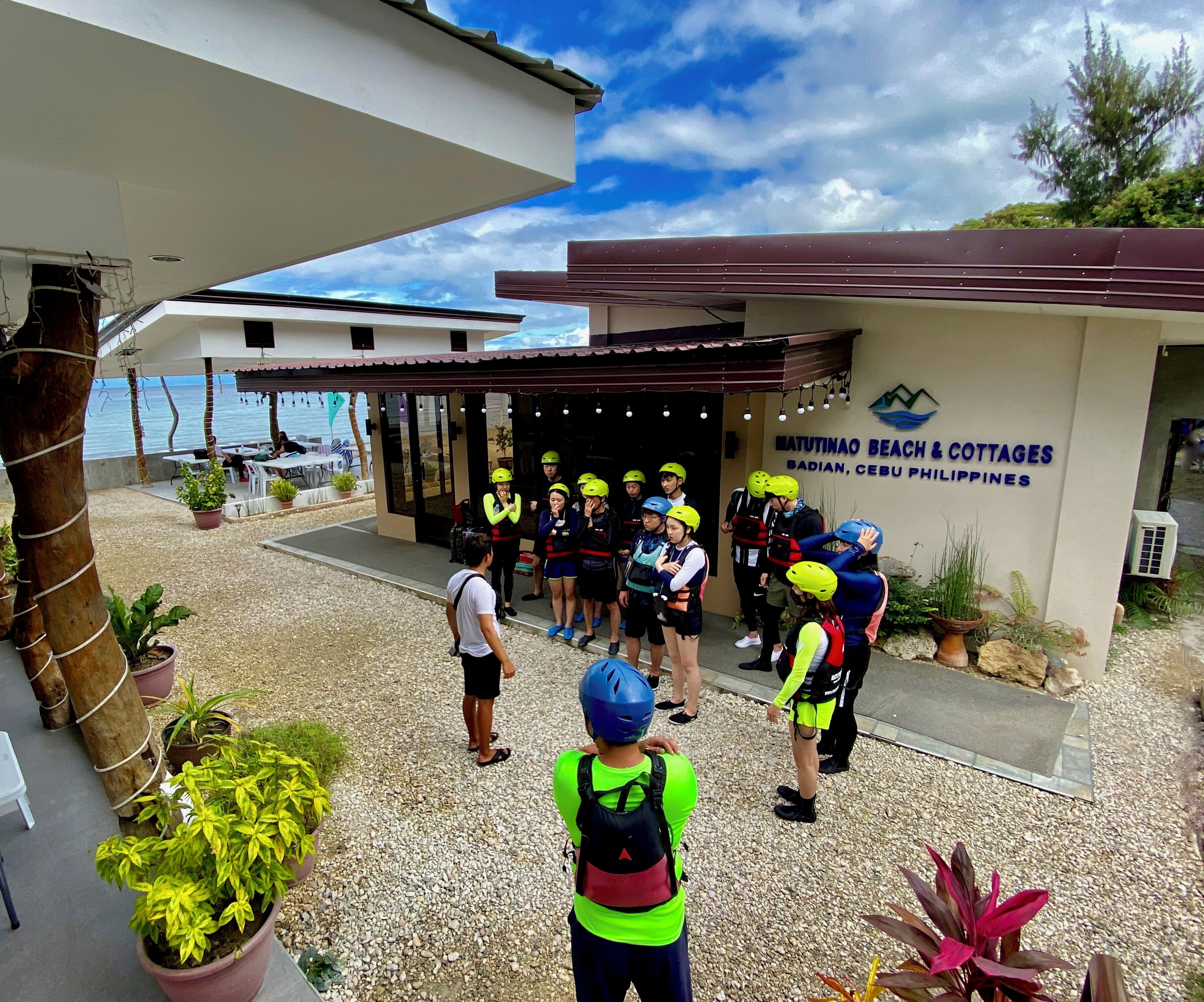 Un grupo de personas con cascos reunidos frente a un edificio con un letrero que dice 'Matutinao Beach & Cottages'.