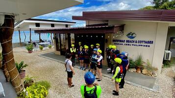Un grupo de personas con cascos reunidos frente a un edificio con un letrero que dice 'Matutinao Beach & Cottages'.