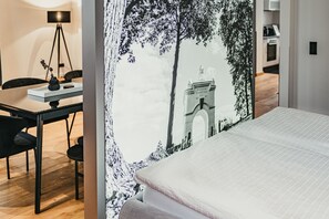 Une chambre d’hôtel avec un lit, un bureau et une chaise. Un mur est décoré d’une fresque représentant un arbre et un bâtiment.