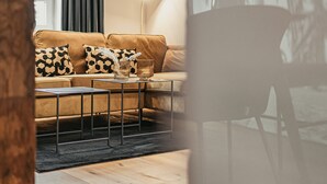 Ein modernes Wohnzimmer mit einer Couch, zwei Beistelltischen, einer Lampe und einem Gemälde an der Wand.