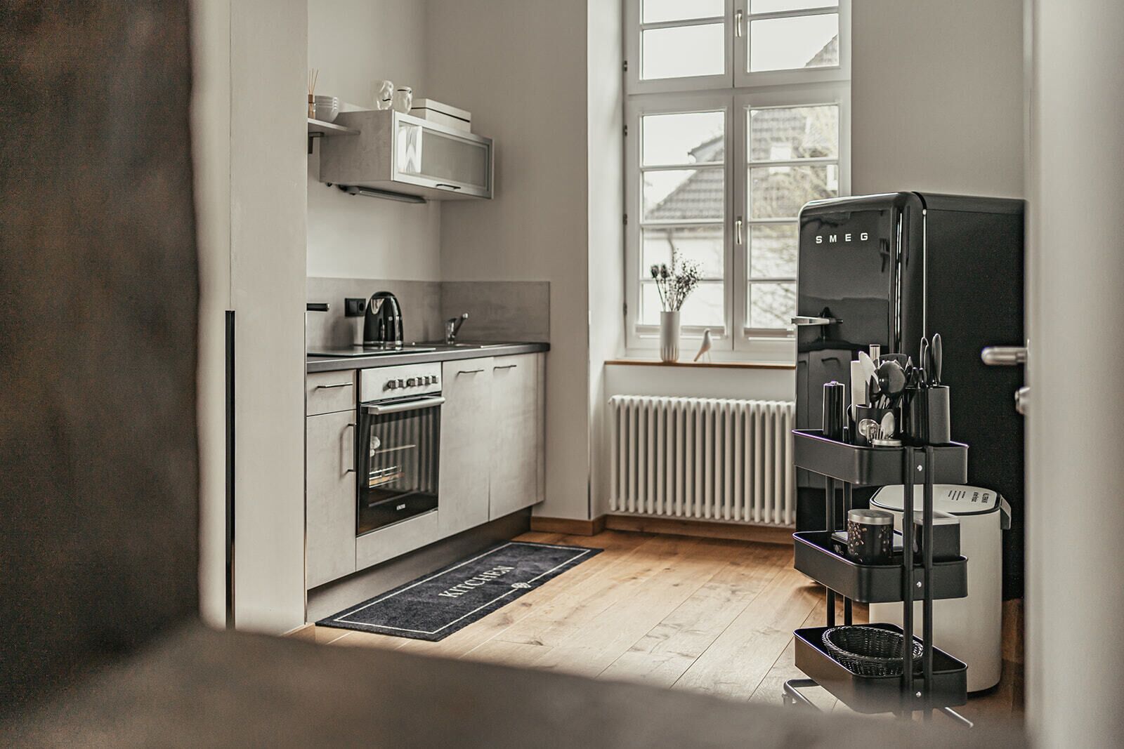 Cozinha moderna com forno embutido, geladeira e janela com vista para uma casa.