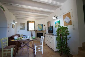 A dining area with a wooden table, chairs, and a white cabinet. There is a plant on the right and a fireplace in the background. - Casale De Li Canti (Salve)