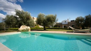 Una piscina limpida con una scultura in pietra, circondata da vegetazione e un edificio sullo sfondo.