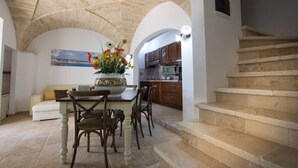 Zona pranzo con tavolo e sedie, un vaso di fiori e una cucina sullo sfondo.